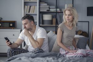 Offended wife looking at her cheating husband with a phone. Crisis in a marriage concept