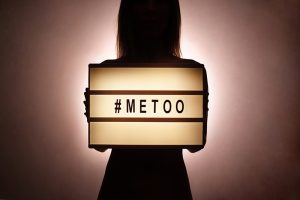 Silhouette of unknown female in the dark covering her chest with #Metoo hashtag word on glowing lightbox. Me too light box. Anti sexism protest movement against inappropriate behavior towards women.